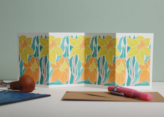 Welsh Daffodil Garland card featuring hand-carved linocut botanical portrait in yellow and orange. Double-sided concertina greeting card with bold, contemporary cottagecore design on eco-friendly recycled cardstock.