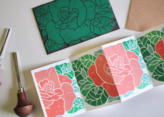 A linocut artwork card featuring a pink red rose with green and teal leaves