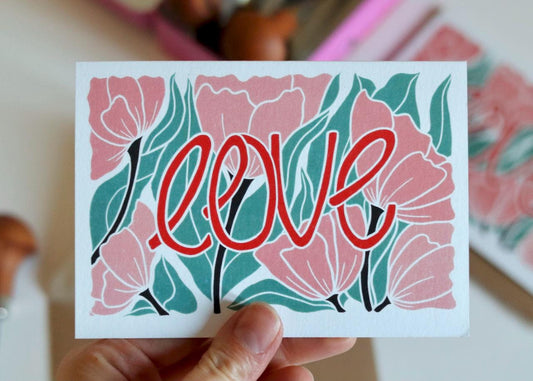 A colourful floral card featuring pink modern flowers, flowing green leaves with the word "love" in a warm red colour. An original design created using linocut.