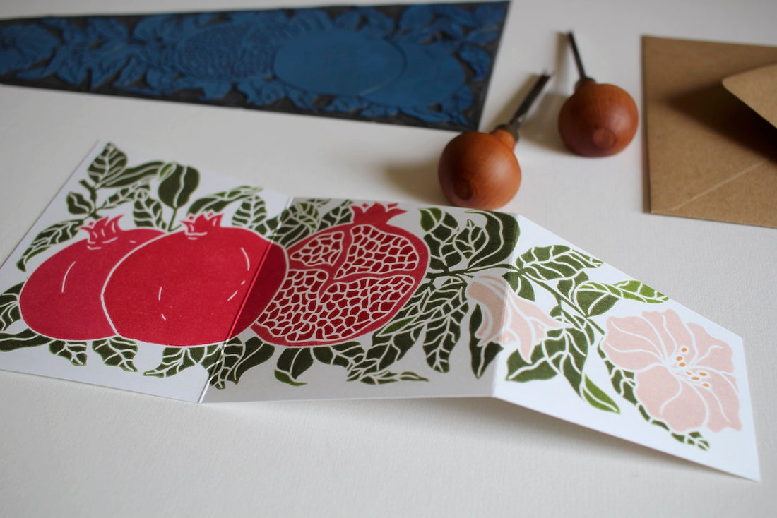 a concertina folded Christmas card featuring a linocut pomegranate design in festive red and green