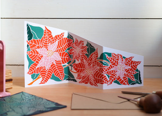 Hand-carved botanical poinsettia festive garland card unfolded on a wooden table