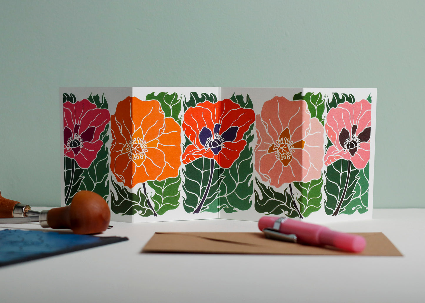 Poppy Parade Garland card featuring hand-carved linocut botanical portrait in pink, orange and red. Double-sided concertina greeting card with bold, contemporary cottagecore design on eco-friendly recycled cardstock.