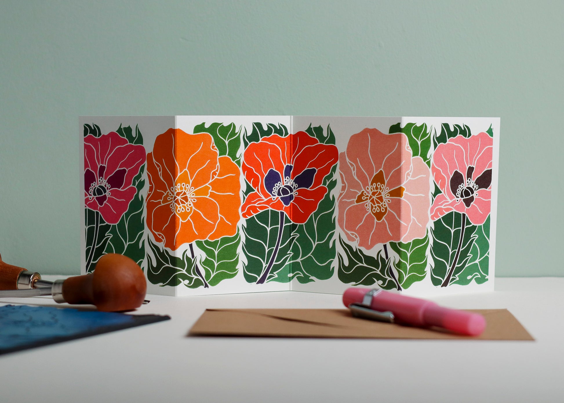 Poppy Parade Garland card featuring hand-carved linocut botanical portrait in pink, orange and red. Double-sided concertina greeting card with bold, contemporary cottagecore design on eco-friendly recycled cardstock.
