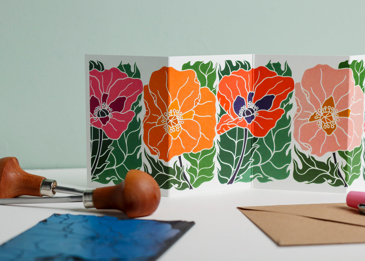 Close-up detail of hand-carved Poppy Parade design on Garland card. Bold orange, pink and red graphic linocut linework showing botanical accuracy and contemporary colour palette inspired by Henri Rousseau and Frida Kahlo.