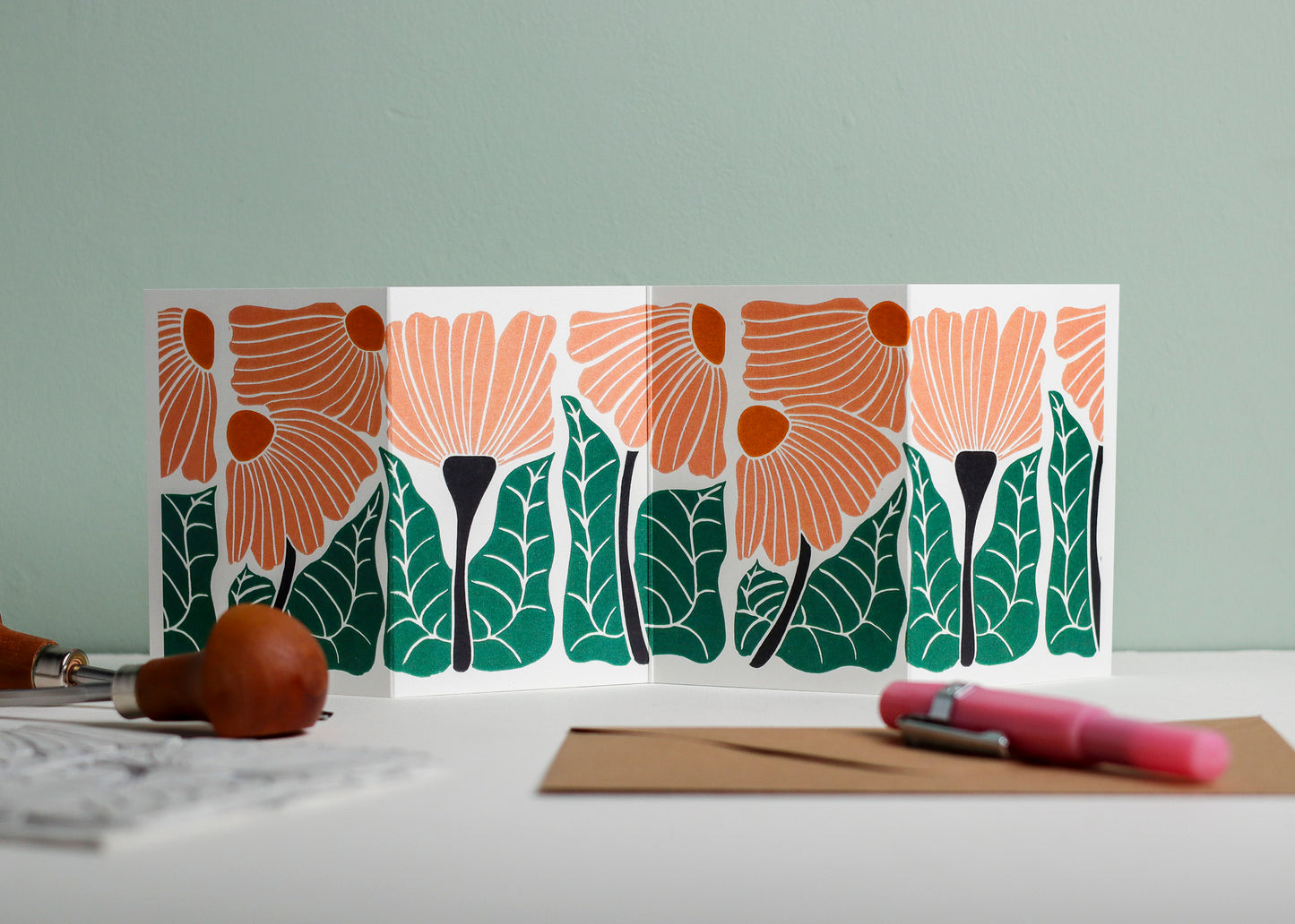 Garden Chorus Garland card featuring hand-carved linocut botanical portrait in peach and green. Double-sided concertina greeting card with bold, contemporary cottagecore design on eco-friendly recycled cardstock.