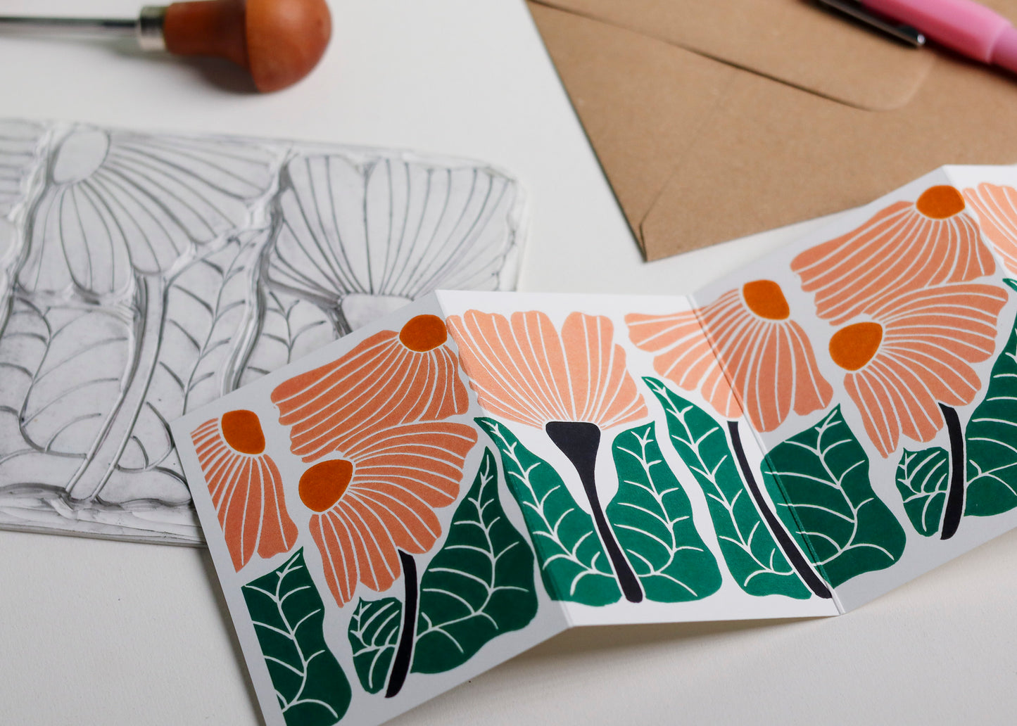 Hand-carved lino block shown beside finished Garden Chorus Garland card. Traditional linocut printmaking tools and original carved linoleum block displayed with contemporary peach botanical portrait card. No AI, authentic craftsmanship from Norfolk studio