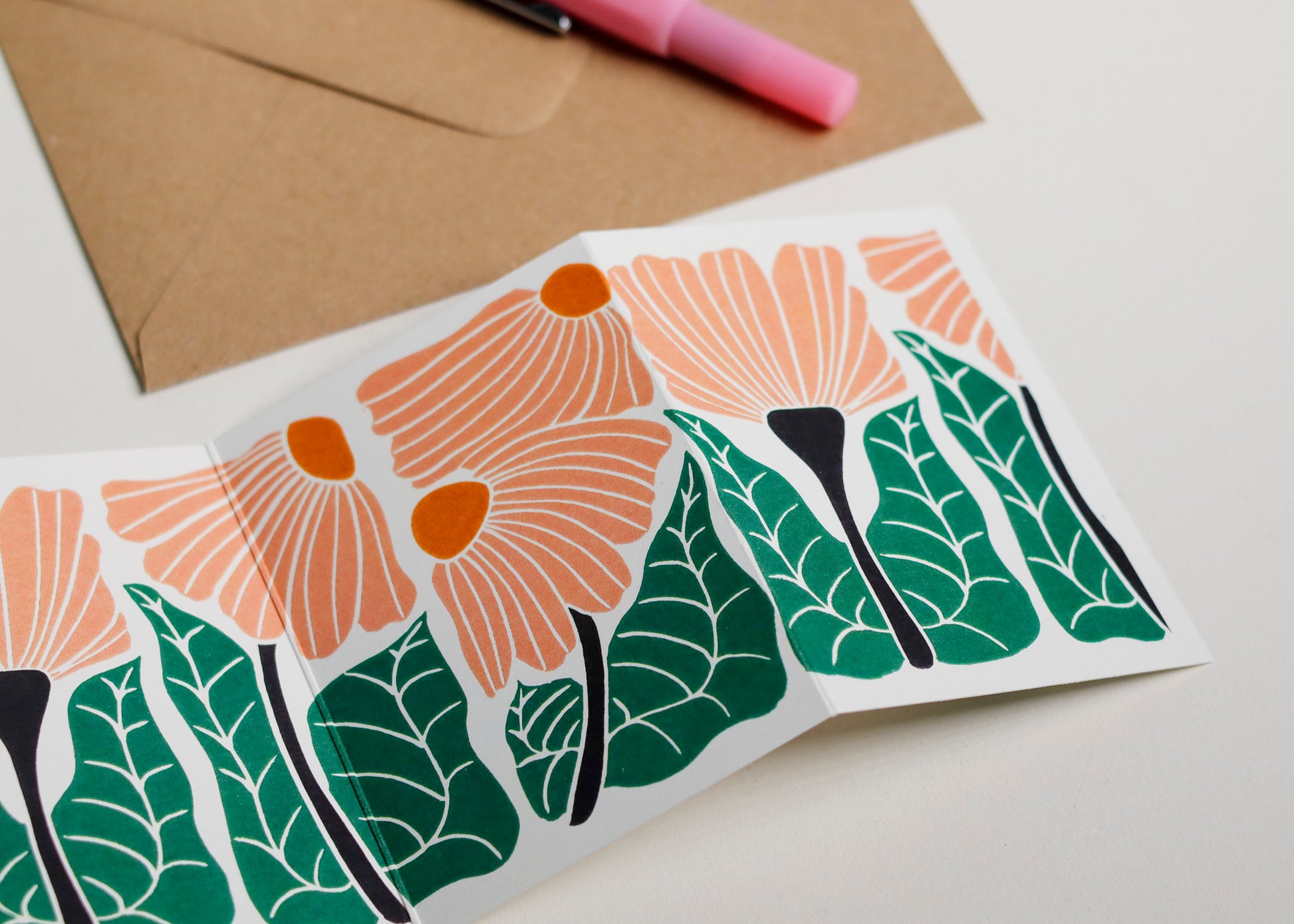 Close-up detail of hand-carved Garden Chorus design on Garland card. Bold peach and green and graphic linocut linework showing botanical accuracy and contemporary colour palette inspired by Henri Rousseau and Frida Kahlo.
