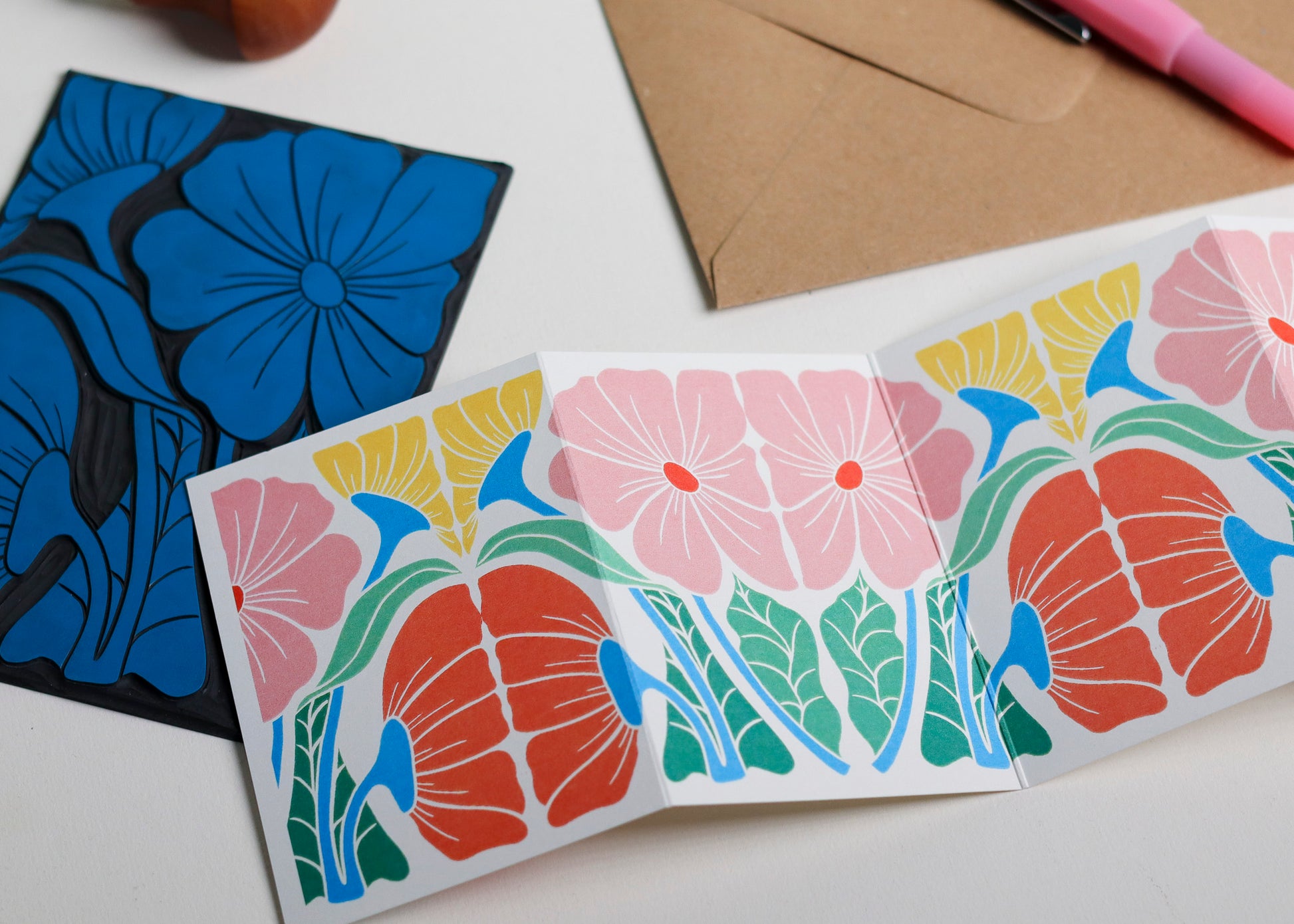 Hand-carved lino block shown beside finished Bright & Beautiful Garland card. Traditional linocut printmaking tools and original carved linoleum block displayed with a contemporary botanical portrait card. No AI, authentic craftsmanship from Norfolk studio.