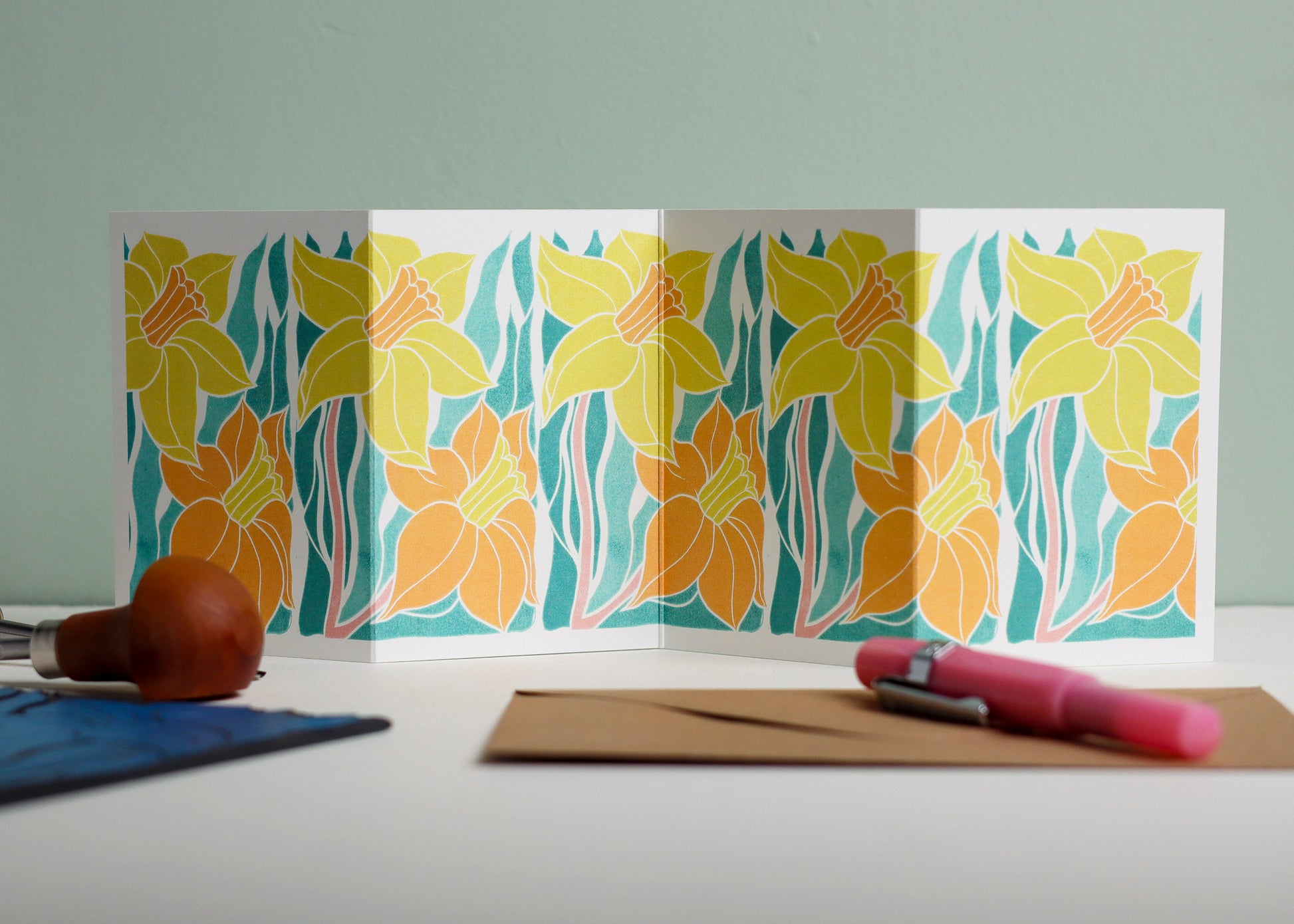 Welsh Daffodil botanical Garland card shown fully extended (105 x 297mm), displaying complete hand-carved linocut design. Modern cottagecore daffodil portrait in yellow and orange, perfect for mantlepiece display.