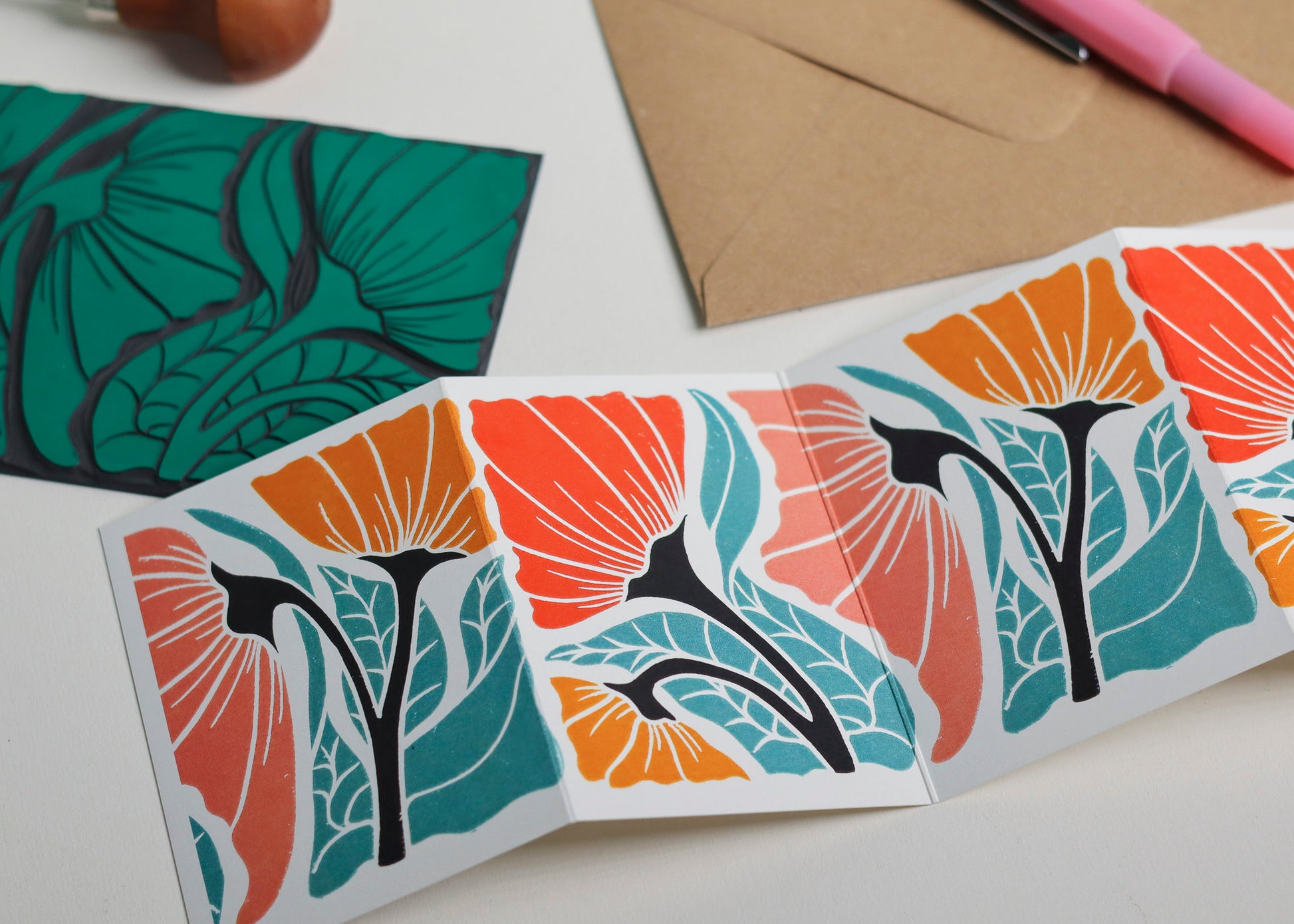 Hand-carved lino block shown beside finished Happy Floral Garland card. Traditional linocut printmaking tools and original carved linoleum block displayed with contemporary abstract floral botanical portrait card. No AI, authentic craftsmanship from Norfolk studio.