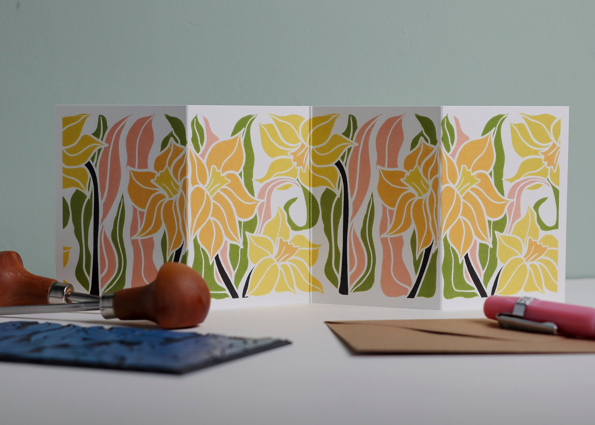 Daffodil botanical Garland card shown fully extended (105 x 297mm), displaying complete hand-carved linocut design. Modern cottagecore daffodil  portrait in pink, green and yellow, perfect for mantlepiece display.