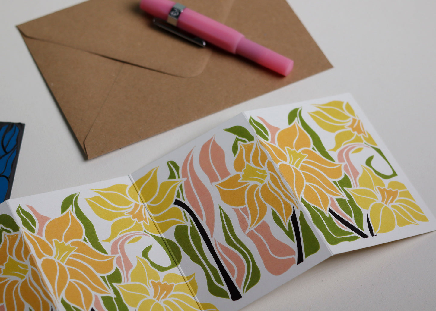 Daffodil Garland card with C6 kraft envelope. Hand-carved botanical portrait greeting card in yellow and pink on recycled cardstock, photographed with eco-friendly envelope, ready for posting.