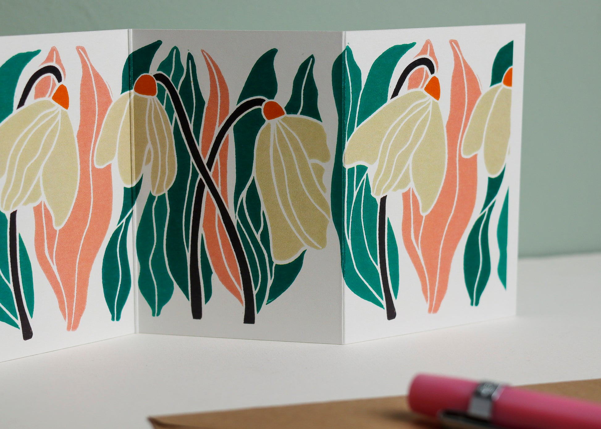 Close-up detail of hand-carved snowdrop design on Garland card. Bold pink and green and graphic linocut linework showing botanical accuracy and contemporary colour palette inspired by Henri Rousseau and Frida Kahlo.