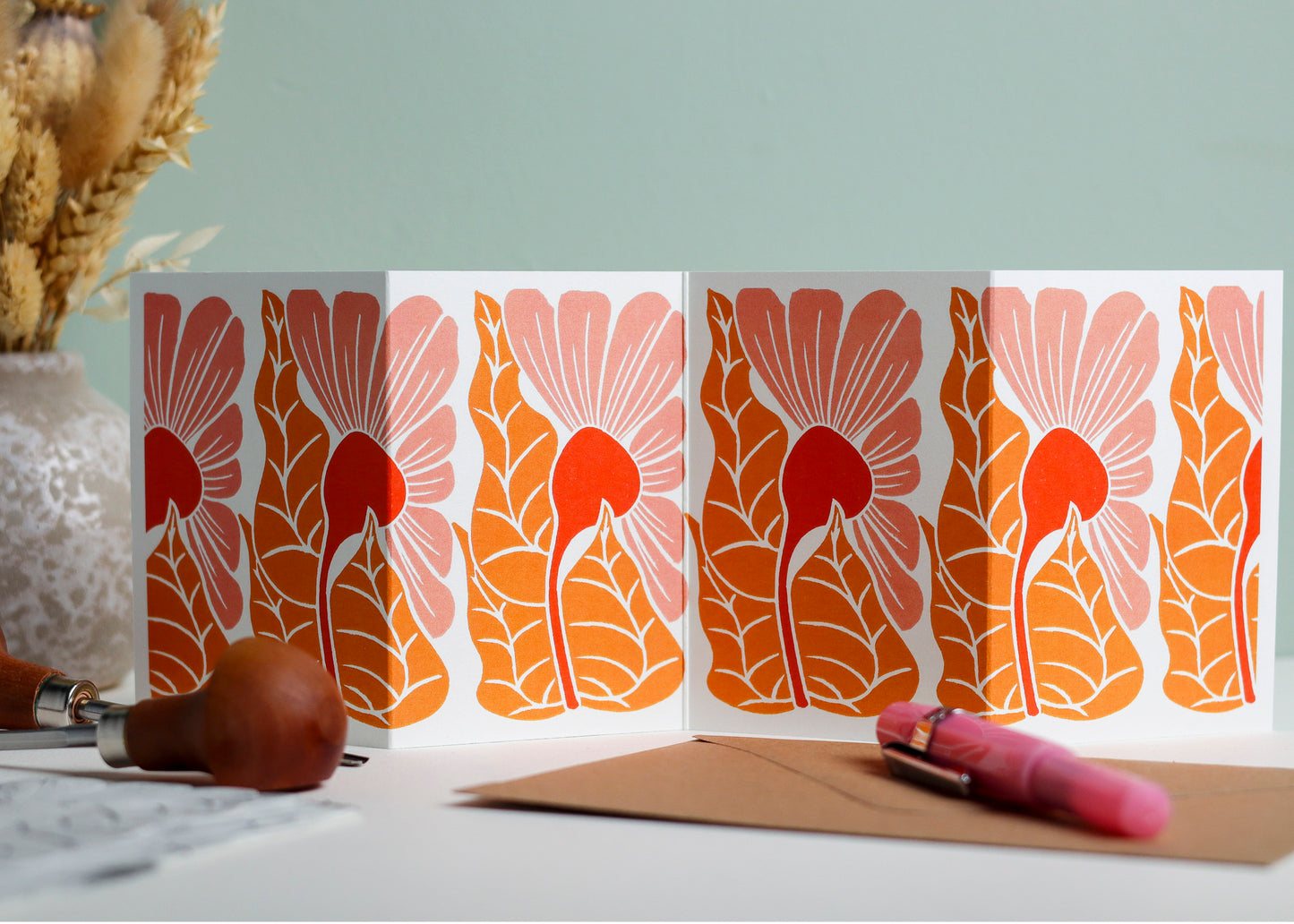 Golden Autumn Garland card featuring hand-carved linocut botanical portrait in warming coral pinks. Double-sided concertina greeting card with bold, contemporary cottagecore design on eco-friendly recycled cardstock