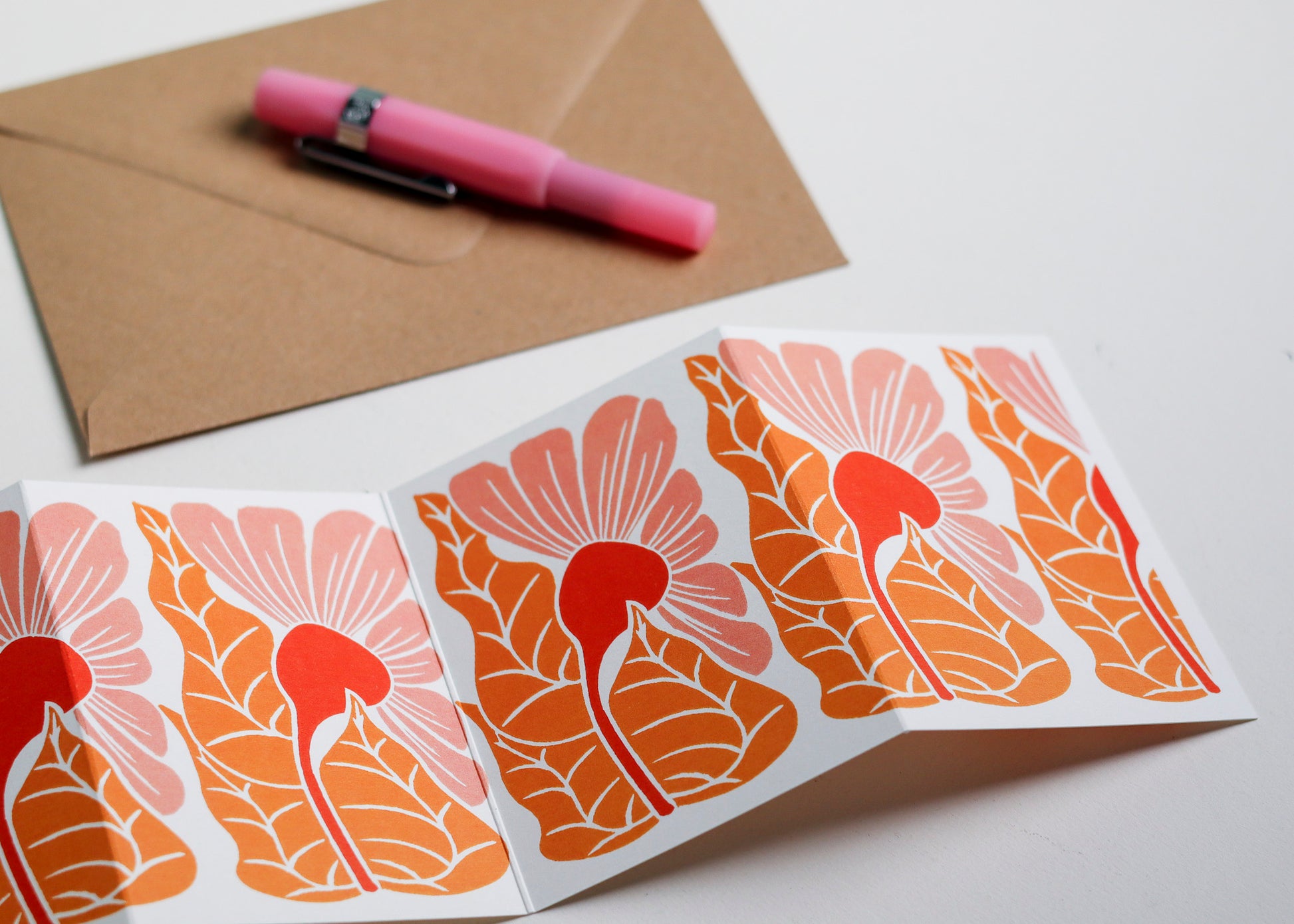 Close-up detail of hand-carved Golden Autumn design on Garland card. Bold coral pink and orange with graphic linocut linework showing botanical accuracy and contemporary colour palette.