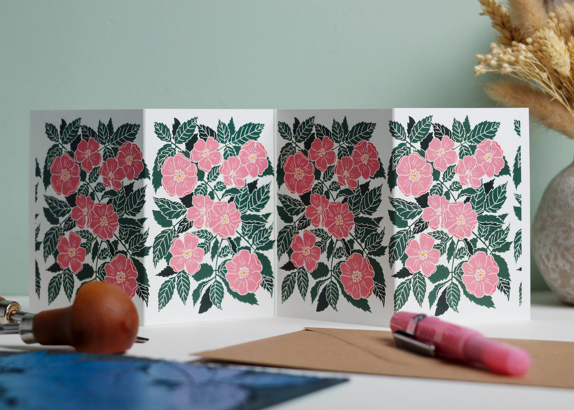Dog Rose botanical Garland card shown fully extended (105 x 297mm), displaying complete hand-carved linocut design. Modern cottagecore wild rose portrait in pink and green, perfect for mantlepiece display
