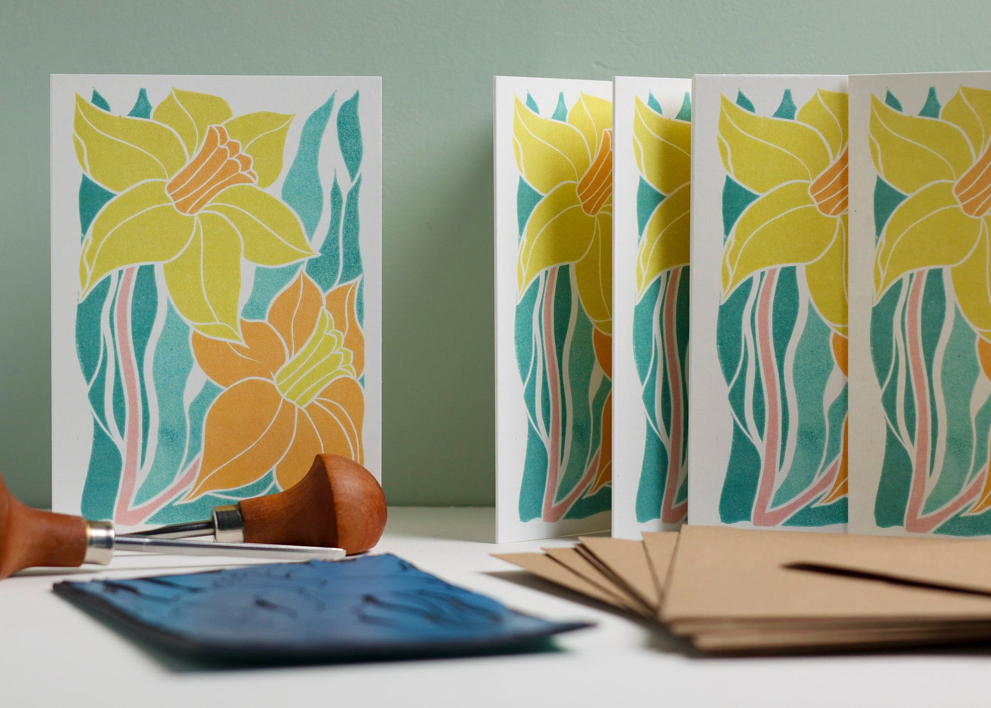 Set of 8 hand-carved botanical notecards featuring the Welsh daffodil, national flower of Wales. A6 linocut print greeting cards in spring yellows and teal, displayed with kraft envelopes. Cottagecore stationery on recycled cardstock.