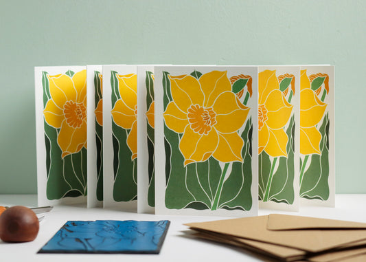 Set of 8 hand-carved botanical notecards featuring the bold and confident spring daffodil. A6 linocut print greeting cards in a classic yellow and green colourway, displayed with kraft envelopes. Cottagecore stationery on recycled cardstock.