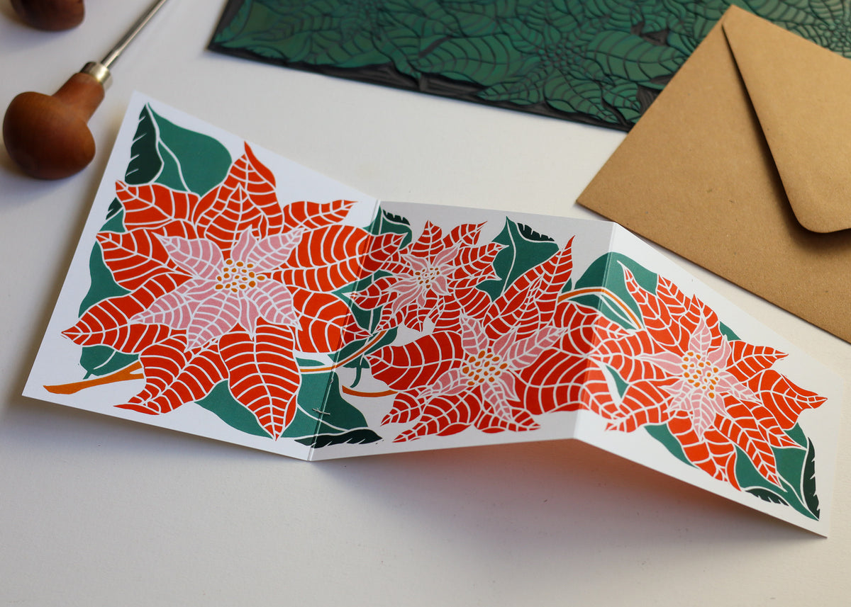 Festive poinsettia garland greeting card displayed flat alongside a kraft paper envelope