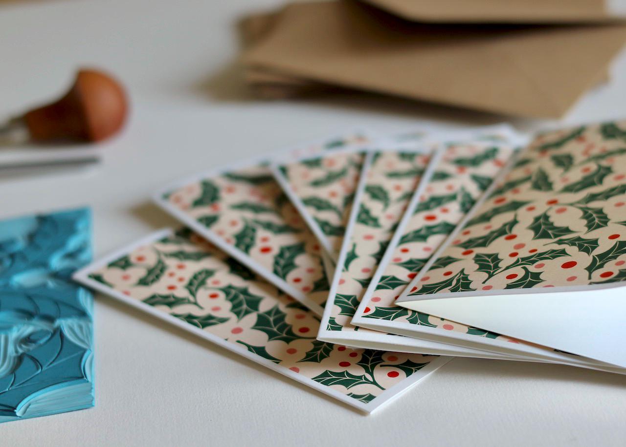 This set of note cards features a repeating festive pattern of holly leaves and polka dot berries in pink and red.