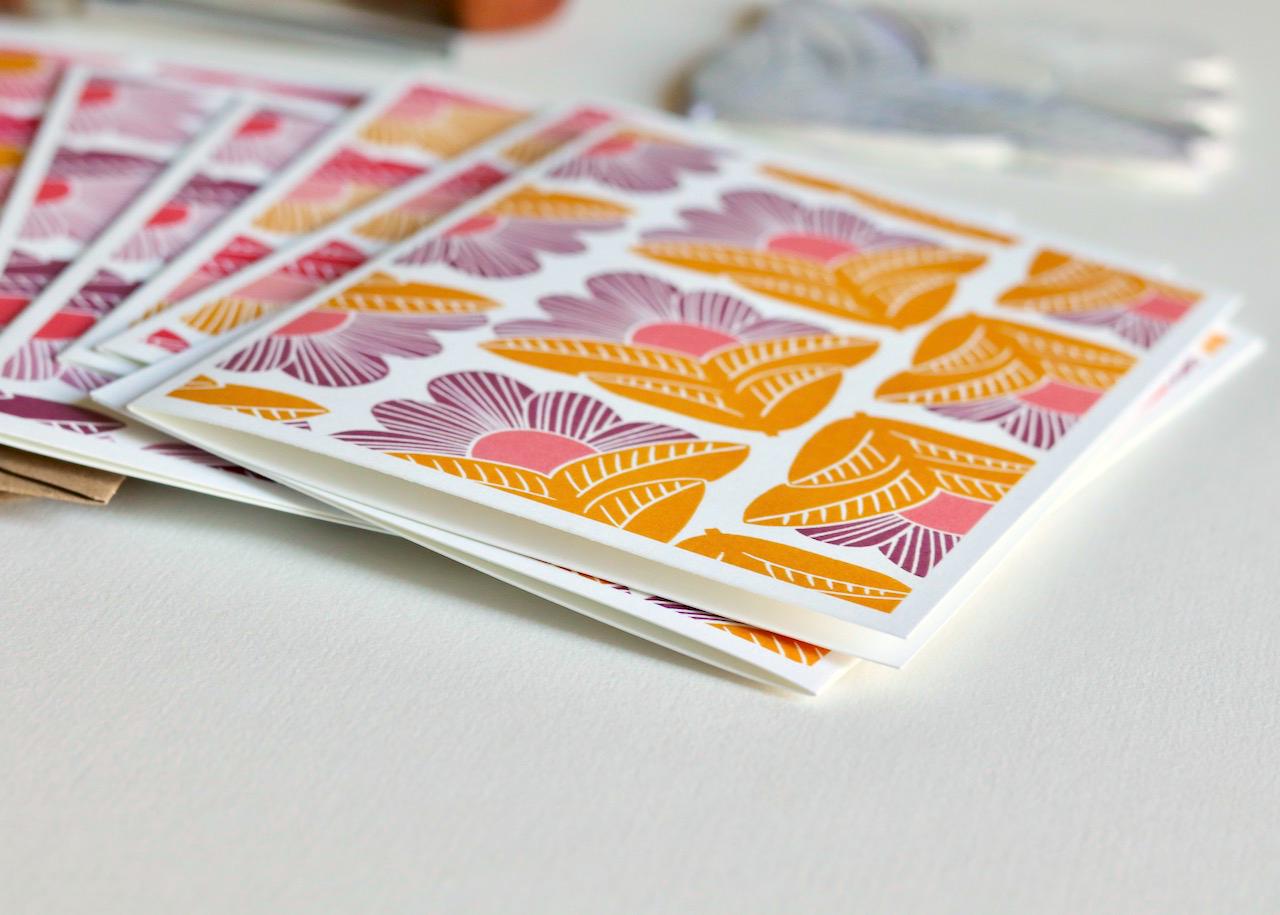 Close-up detail of hand-carved linocut print showing intricate line work within geometric flower petals, printed in vibrant pink and golden yellow